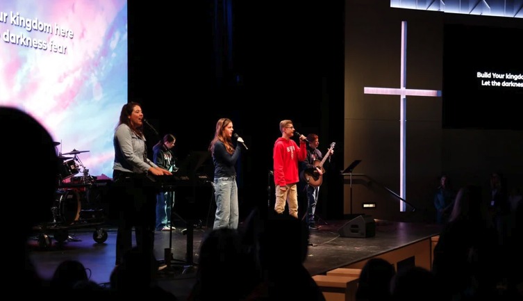 Trinity students leading worship on stage with a glowing cross behind them