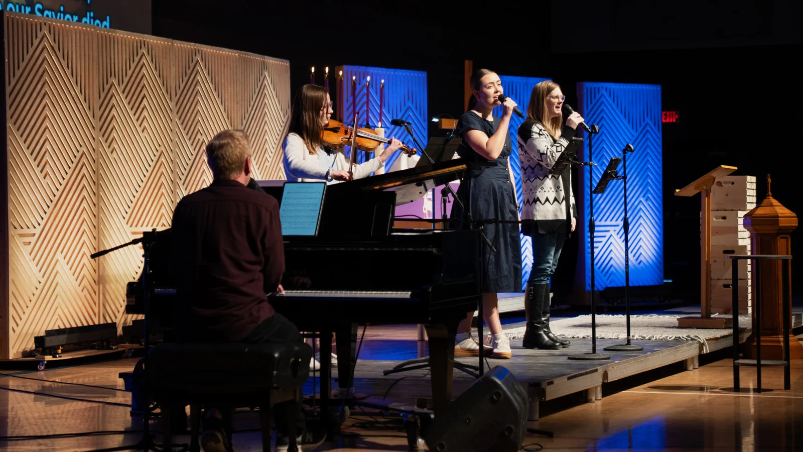 Trinity worship team leading music on the sanctuary stage — piano, violin, and vocalists