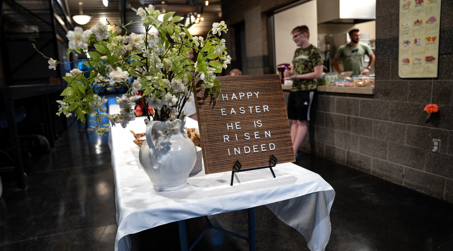 A coffee fellowship table set for a Sunday morning, with a letterboard reading Happy Easter, He Is Risen Indeed