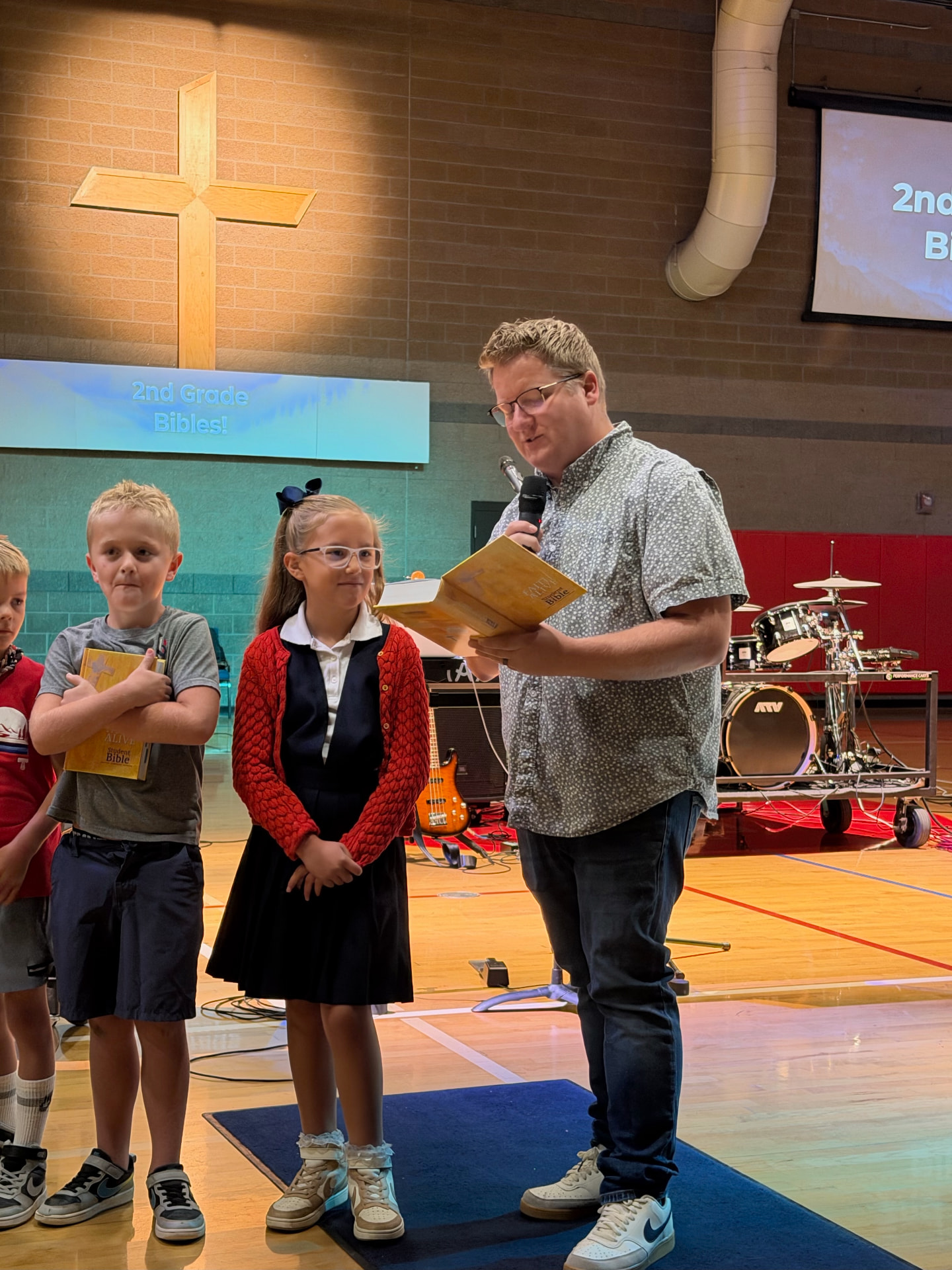 A Trinity pastor presenting a Bible to second grade students in the gym