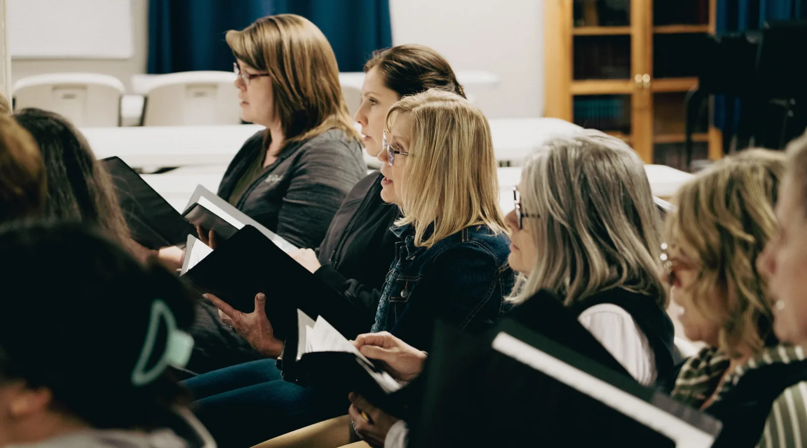 Trinity choir members holding their music folders as they sing in rehearsal