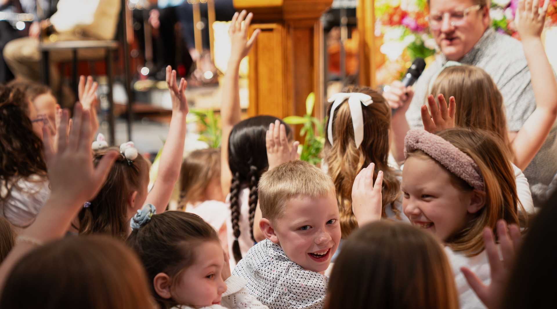 Smiling children raising their hands during a children's message at Trinity