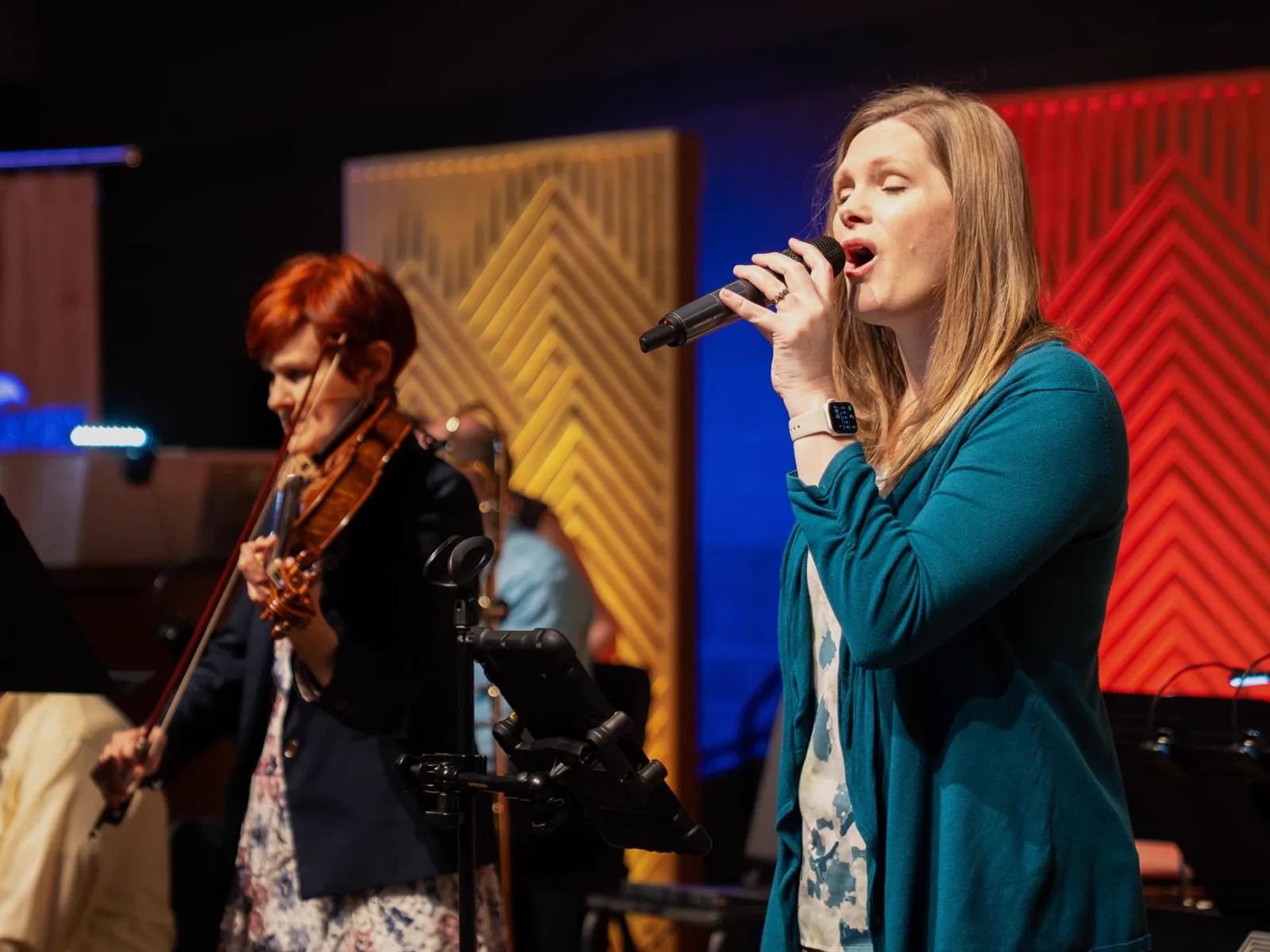 A Trinity vocalist singing into a microphone while a violinist plays beside her on stage